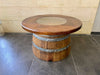 Wooden barrel table with a round top on a tiled floor.