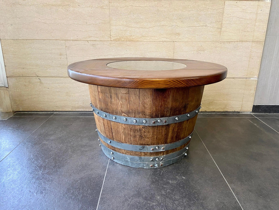 Wooden barrel table with metal bands on a tiled floor against a beige wall.