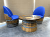 Wooden barrel-style table with two matching chairs featuring blue cushioned seats on a tiled floor.
