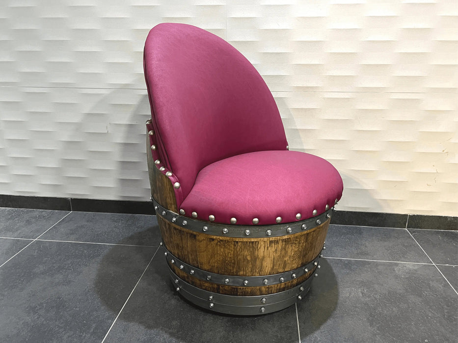Chair made from a wine barrel with pink cushion and metal studs against a light wall.