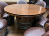 Wooden barrel-style table with round top and studded design, surrounded by matching chairs.