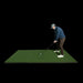 Person practicing golf on a green mat with a black background
