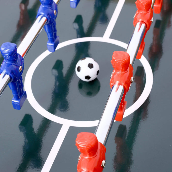 Close-up of a table football game with red and blue player figures and a white ball on a reflective surface.