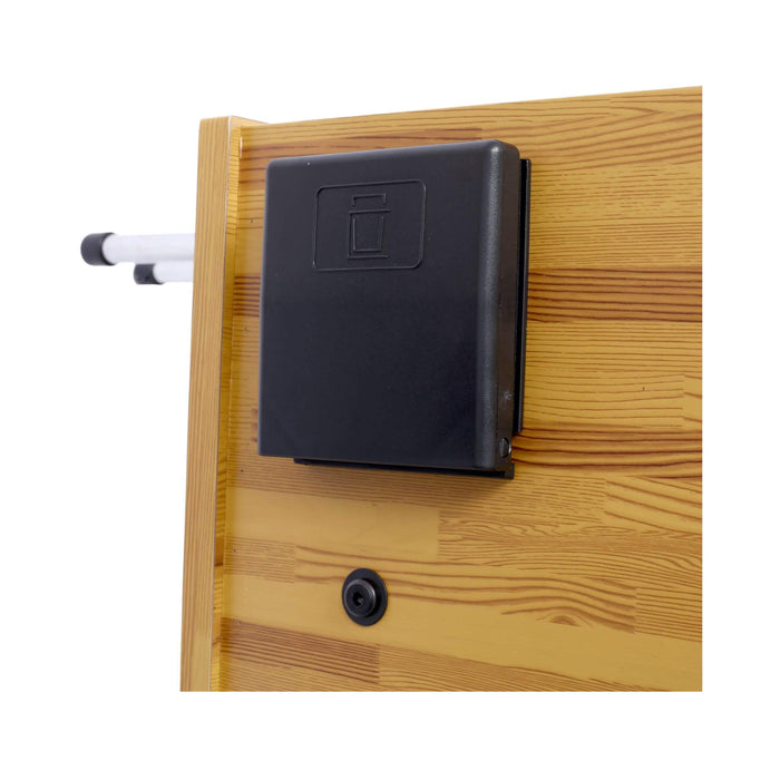 Black rectangular device attached to a wooden surface with a white pipe-like object on the left.