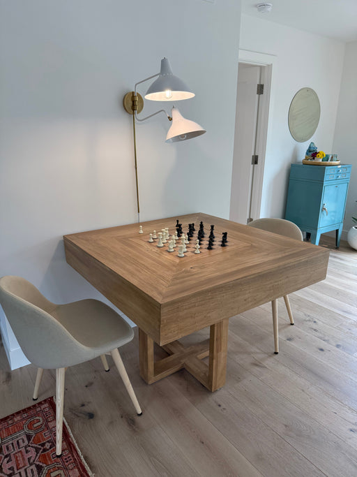 Wooden dining table with chess pieces in a room with a lamp and chairs.