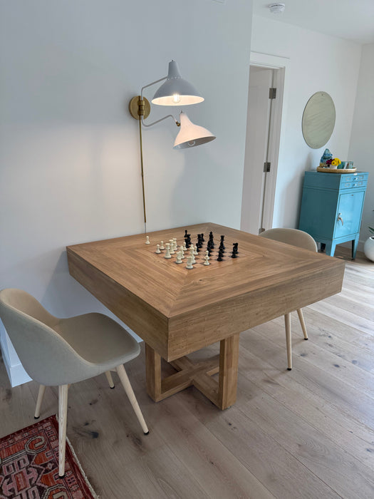 Wooden dining table with chess pieces in a room with a lamp and chairs.