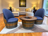 Two blue cushioned chairs around a wooden barrel table in a living room setting.