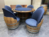 Wooden barrel chairs with blue cushions around a round wooden table on a tiled floor.
