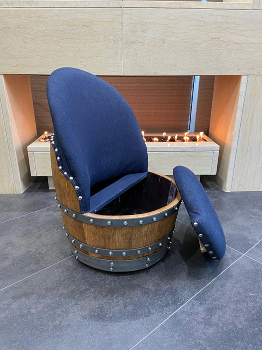 Chair made from a wooden barrel with blue cushioned seat and backrest on a tiled floor.
