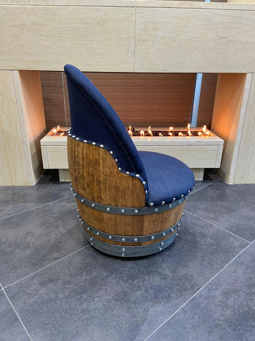 Chair made from a wine barrel with a blue cushion in front of a fireplace.
