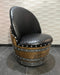 Chair made from a repurposed wine barrel with black leather seat against a neutral wall.