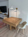 Wooden dining table with two chairs in a room with a television and lamp.