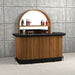 Portable bar with wooden design and black top against a concrete wall.