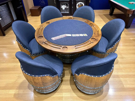 Wooden poker table with blue felt surface surrounded by matching chairs in a room with a pool table.