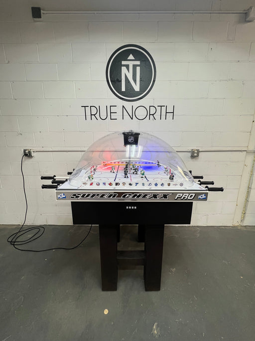 Super Game Pro air hockey table with 'True North' branding on a white brick wall.