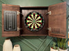 Wooden dartboard cabinet with a dartboard inside, on a green wall background.