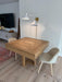 Wooden dining table with two chairs in a room with a television and lamp.