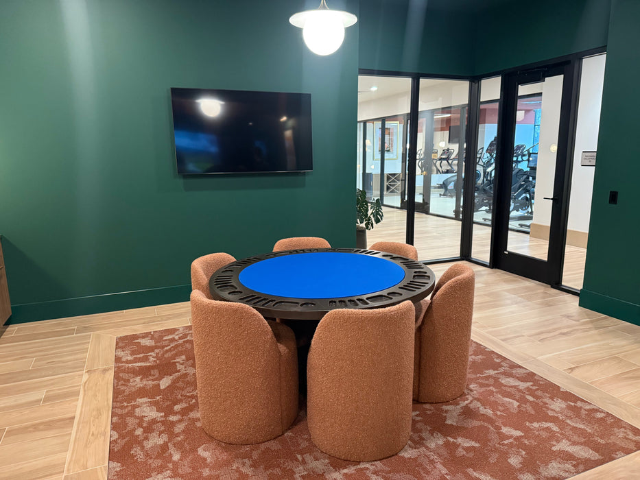 Round table with blue top surrounded by chairs in a room with green walls and a TV.