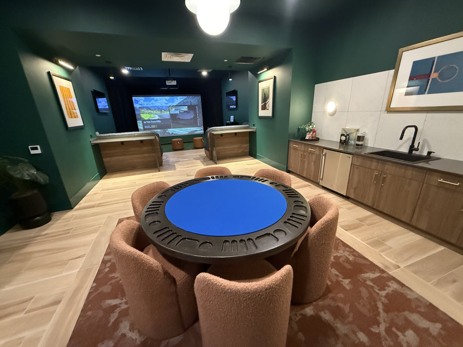 Game room with a blue poker table and chairs, TV, and kitchen area.