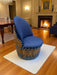 Chair made from a wooden barrel with blue cushioned seat in a room with a fireplace.
