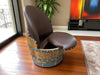 Brown leather chair with wooden base in a room with a painting on the wall.