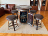 Bar setup with wine barrel table and stools in a room with a couch and bookshelf.