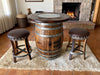 Wooden barrel table with two stools in a cozy room with a fireplace.