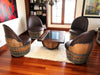 Wooden barrel chairs around a coffee table in a room with a bookshelf and window.