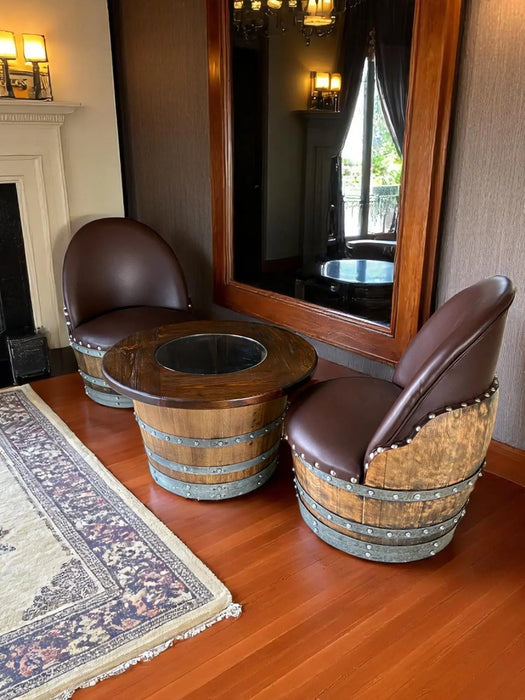 Two barrel chairs with a table in front of a large mirror in a room.