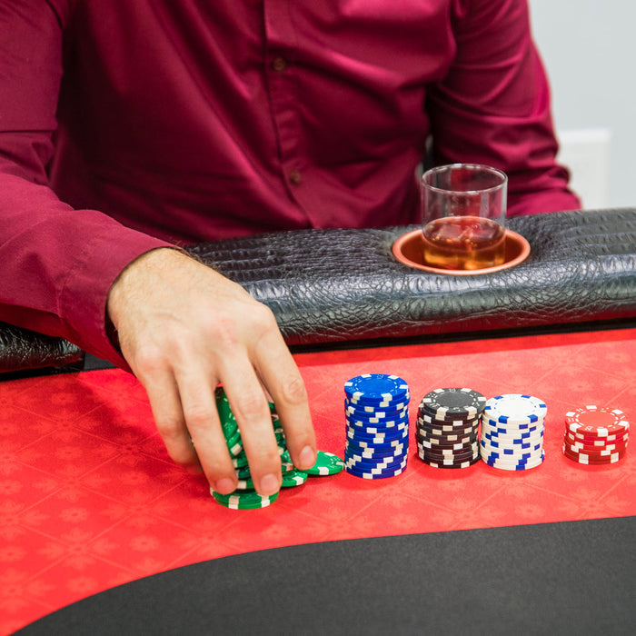 Person playing poker with colorful chips on a red and black table.