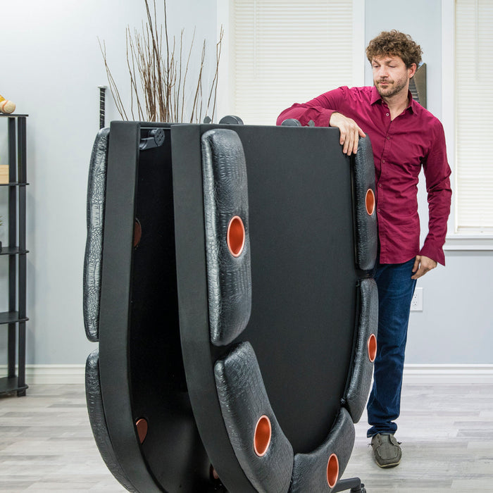 Man lifting a large black massage chair in a room with light-colored walls and flooring.