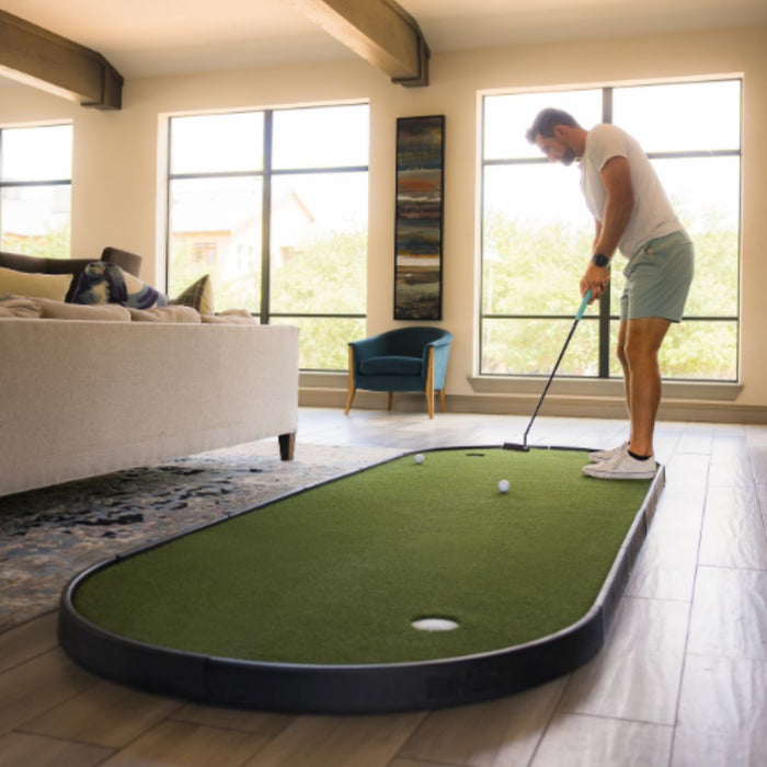 Man playing mini golf in a living room with large windows.