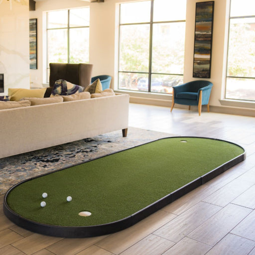 Miniature golf putting green set up in a living room with furniture and large windows.
