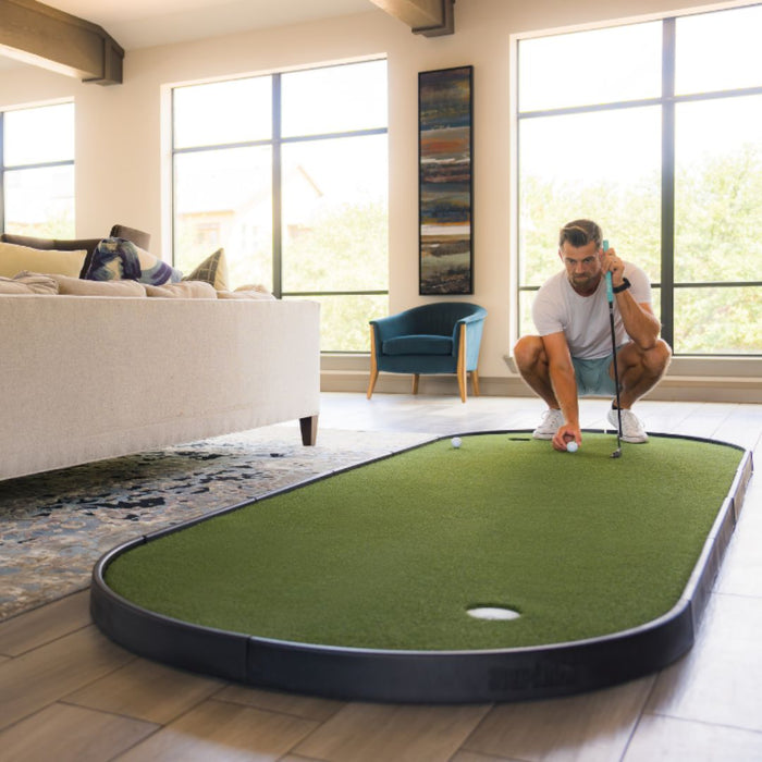 Man playing mini golf on a green mat in a living room.