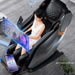 Woman using a massage chair with Bluetooth music display and smartphone on a gray floor.