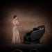 Woman in a glamorous dress standing next to a black massage chair against a brown background