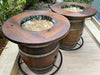 Two wooden barrel planters on a patio with plants in the background