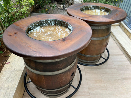 Two wooden barrel planters on a patio with plants in the background