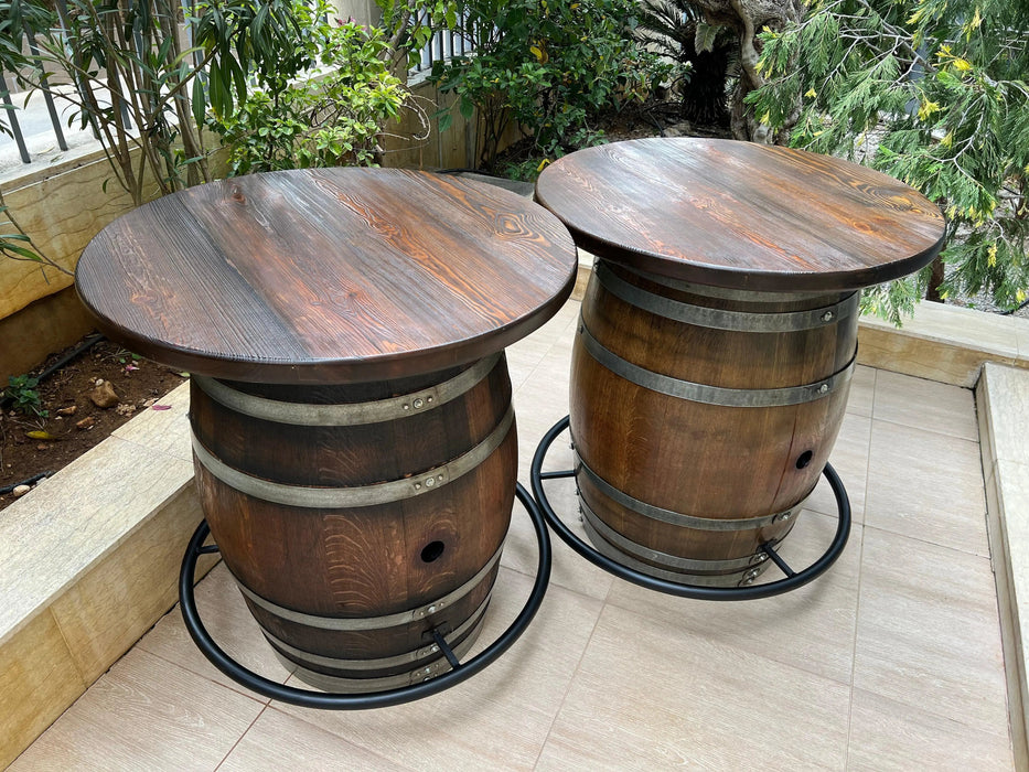 Two wooden barrel tables on a patio with plants in the background