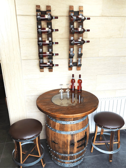 Wooden barrel table with wine bottles and stools against a wall with wine bottle racks.
