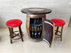 Bar made from a wine barrel with red cushioned stools on a light tiled floor.