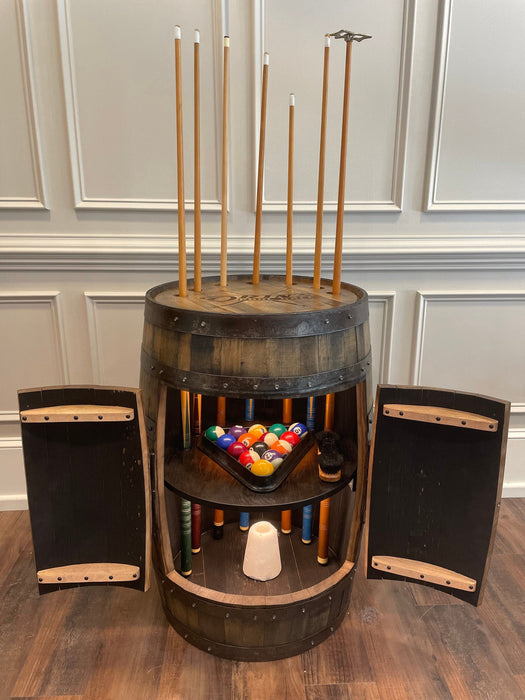 Wooden barrel-shaped pool table with cue sticks, balls, and accessories on a wooden floor.