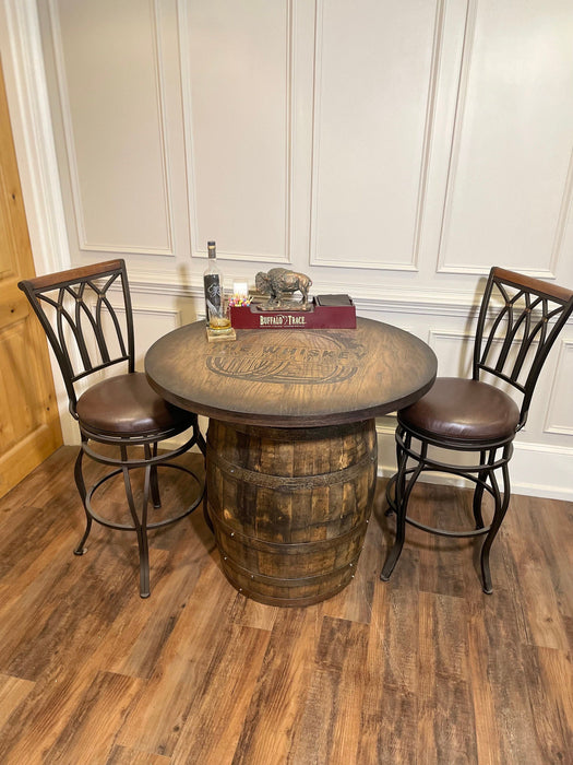 Wooden barrel table with two bar stools in a room with white paneled walls.