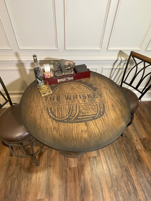 Wooden table with 'The Whiskey Workshop' branding in a room with chairs and decor.