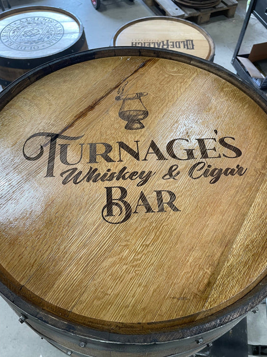 Wooden barrel with 'Turnage's Whiskey & Cigar Bar' engraving on a concrete floor.