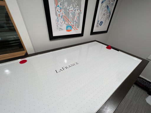 Air hockey table with 'LaFrance' branding in a room with framed artwork on the wall.
