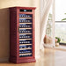 Red wine cooler with bottles inside in a room with a window and plant