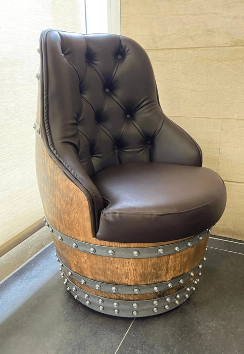 Brown leather chair on a wooden barrel with metal studs against a beige wall.