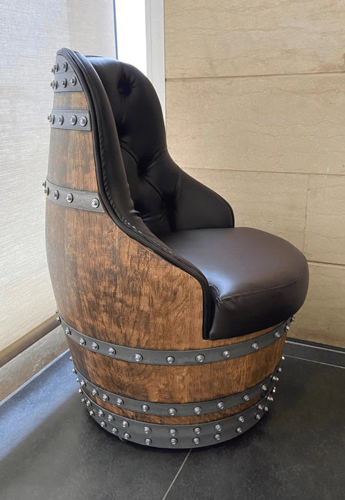 Chair made from a repurposed wine barrel with black cushioned seat against a neutral wall.