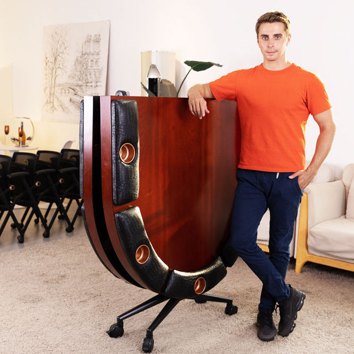 Man standing next to a large wooden and black chair in a room with furniture and decor.